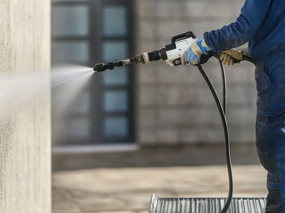Reinigungskraft reinigt Gebäudefassade mit Hochdruckreiniger und entfernt Verschmutzungen von Außenwand. Klicke auf das Bild, um auf die Seite Fassadenreinigung zu kommen.